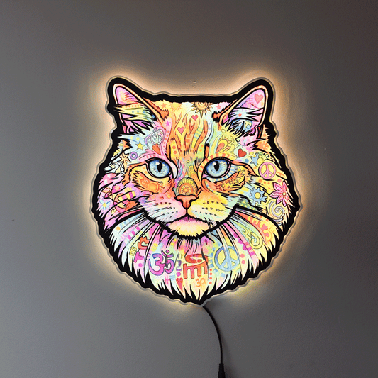A colorful LED wall light shaped like a cat's face, featuring a vibrant multicolor paisley and floral pattern with blue eyes, glowing against a dark gray wall.