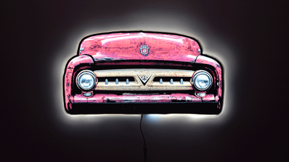 A 1953 F100 front grill wall light, shown against a dark background with a glowing white outline around the illuminated edges.  Front grille with round headlights and a small Ford crest emblem at the top center and a V8 emblem in the center of the classic toothy truck grille with power cord hanging from the bottom.
