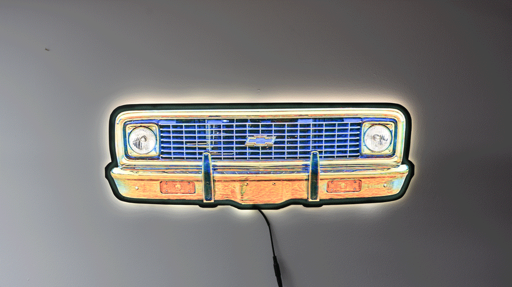 A neon-style wall light of a K10 front grille, glowing with blue, orange, yellow, and white light against a plain gray wall.