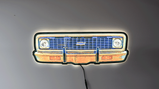 A neon-style wall light of a K10 front grille, glowing with blue, orange, yellow, and white light against a plain gray wall.