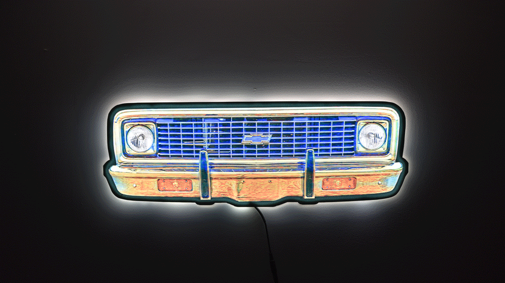 A neon sign depicting a 1970 K10 front grille, featuring a glowing blue grille, chrome bumper, and white headlight glow, set against a dark background.