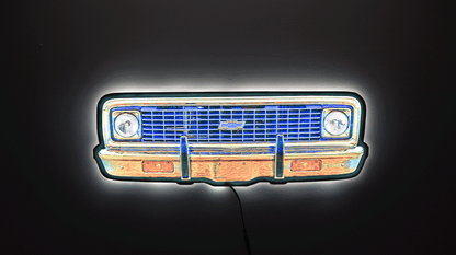 A neon sign depicting a 1970 K10 front grille, featuring a glowing blue grille, chrome bumper, and white headlight glow, set against a dark background.
