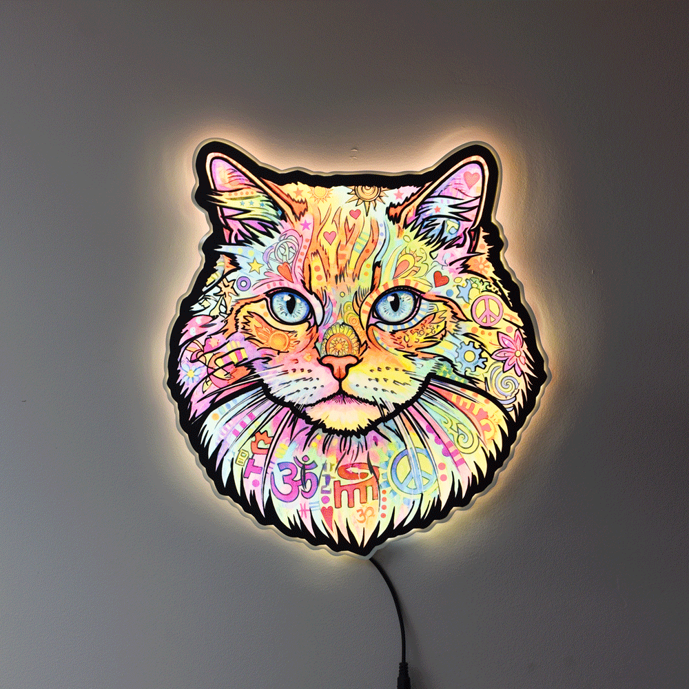 A colorful LED wall light shaped like a cat's face, featuring a vibrant multicolor paisley and floral pattern with blue eyes, glowing against a dark gray wall.