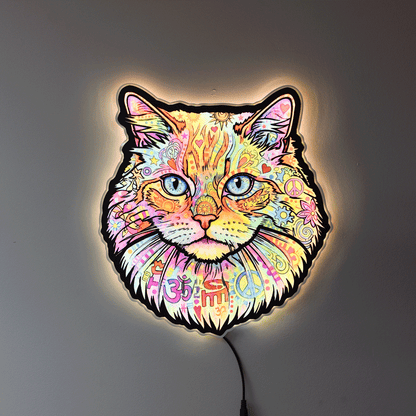 A colorful LED wall light shaped like a cat's face, featuring a vibrant multicolor paisley and floral pattern with blue eyes, glowing against a dark gray wall.