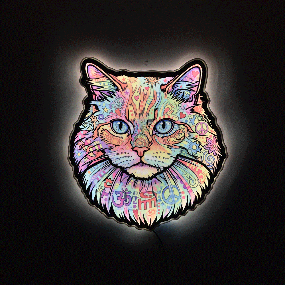 A glowing LED light sign shaped like a cat's face, decorated with a colorful psychedelic pattern of flowers, peace signs, hearts, and swirls, set against a dark background.