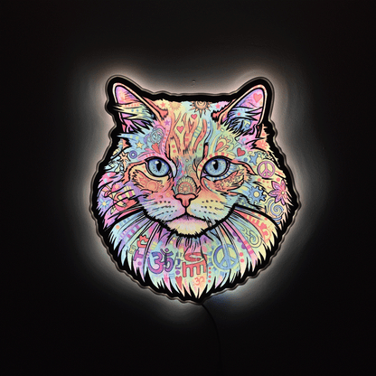 A glowing LED light sign shaped like a cat's face, decorated with a colorful psychedelic pattern of flowers, peace signs, hearts, and swirls, set against a dark background.