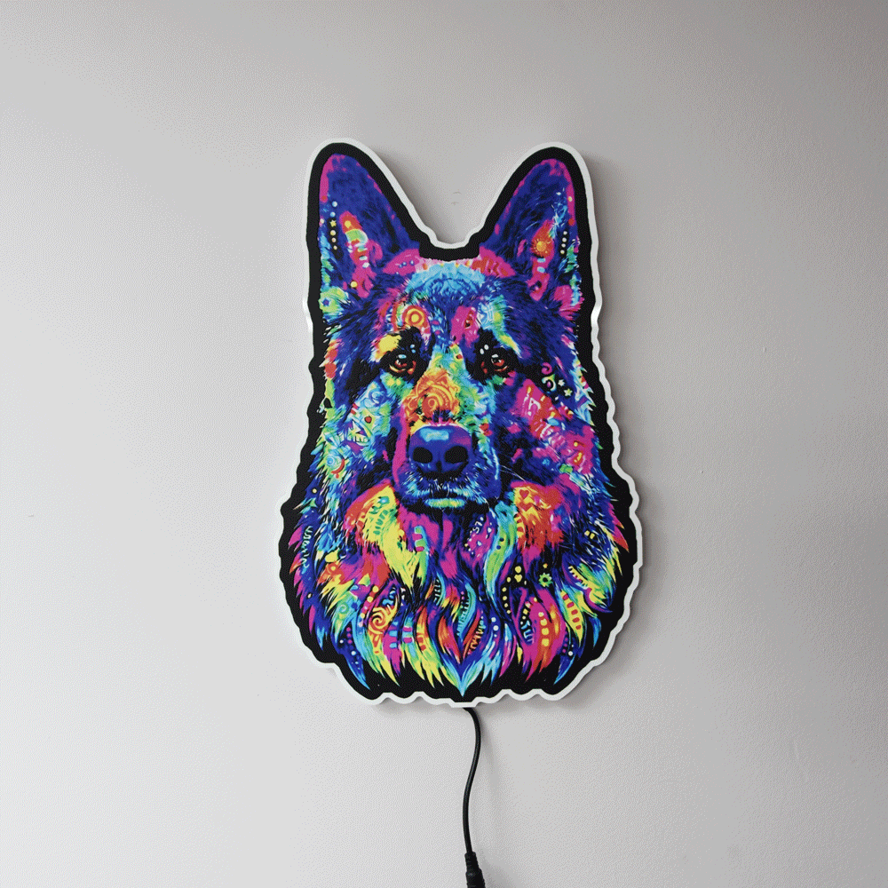 A colorful LED wall light shaped like a German Shepherd dog's face, featuring a vibrant neon pattern in blue, pink, purple, yellow, and green, mounted on a plain light gray wall.