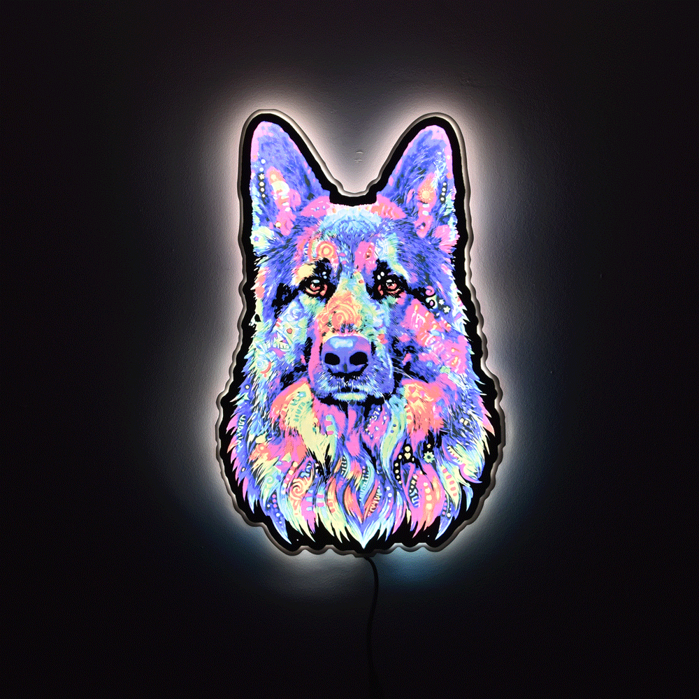 A glowing LED neon sign shaped like a German Shepherd dog face, featuring a vibrant multicolor neon pattern of pink, blue, purple, and yellow on a black backing, set against a dark background.