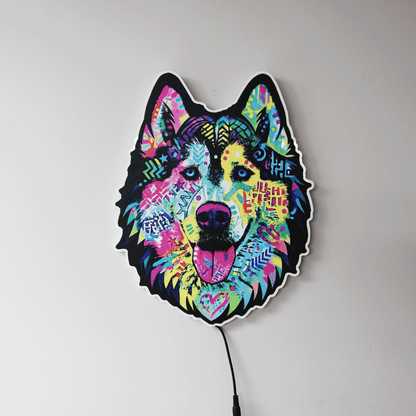 A colorful LED light shaped like a dog's head, featuring a vibrant, multicolored graffiti-style design on a black base, shown against a plain light gray wall with a power cord visible.