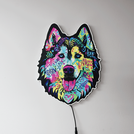 A colorful LED light shaped like a dog's head, featuring a vibrant, multicolored graffiti-style design on a black base, shown against a plain light gray wall with a power cord visible.