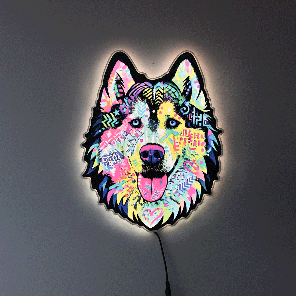 A colorful LED wall light shaped like a wolf or husky head, glowing against a dark gray wall. The design features a vibrant, multicolored graffiti-style pattern with pink, blue, yellow, and green details, and a black outline.