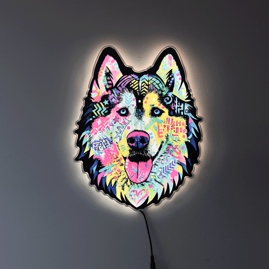 A colorful LED wall light shaped like a wolf or husky head, glowing against a dark gray wall. The design features a vibrant, multicolored graffiti-style pattern with pink, blue, yellow, and green details, and a black outline.