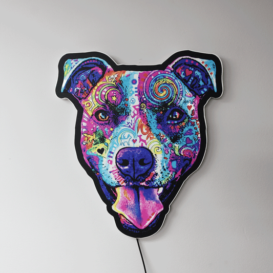 A wall art piece shaped like a Colorful Smiling Pit Bull Face with tongue hanging out, featuring a vibrant psychedelic pattern in shades of purple, blue, pink, yellow, and green, mounted on a plain light gray wall.