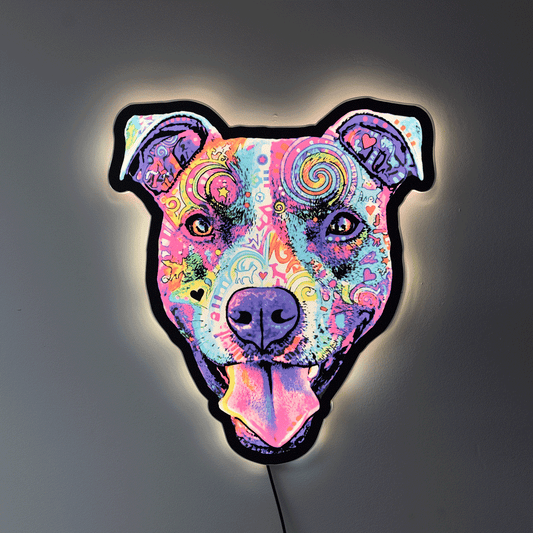 A decorative light shaped like a Colorful Smiling Pit Bull Face with tongue hanging out, featuring a vibrant psychedelic pattern in pink, purple, blue, yellow, and green, with a glowing warm white light around the edges, mounted on a dark gray wall.