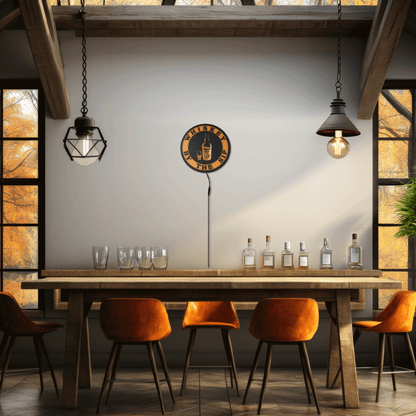 Whiskey By The Sip sign above Home bar area with wooden table, orange chairs, and wall clock in a rustic setting.