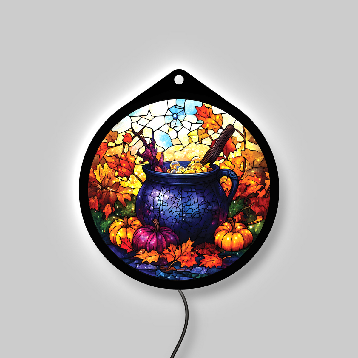 Witch's cauldron LED sign glowing on a wall, pumpkins and fall leaves lit up in a lit room