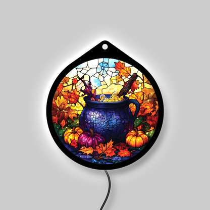 Witch's cauldron LED sign glowing on a wall, pumpkins and fall leaves lit up in a lit room