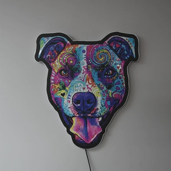 A pop-art style Colorful Smiling Pit Bull Face with tongue hanging out wall light turned on and off, glowing against a dark background when on in a dark room. The design features swirling patterns and bright neon-like colors including pink, purple, blue, yellow, and orange.