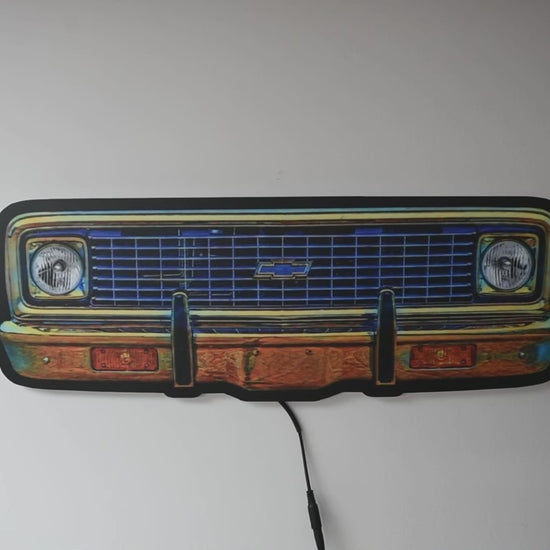 A neon sign depicting a 1970 K10 front grille, demonstrating when the light is off and then turned on showing a glowing blue grille, chrome bumper, and white headlight glow, set against a dark background.