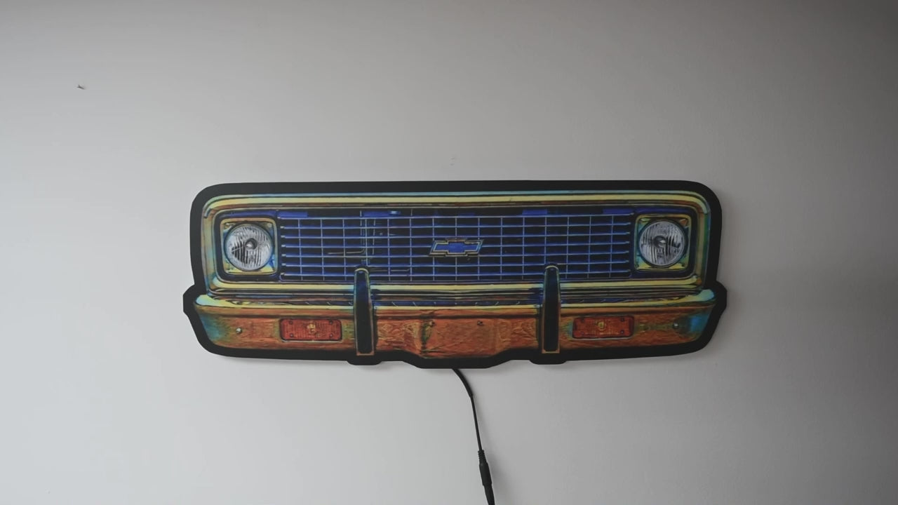 A neon sign depicting a 1970 K10 front grille, demonstrating when the light is off and then turned on showing a glowing blue grille, chrome bumper, and white headlight glow, set against a dark background.