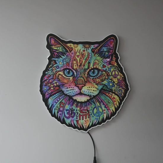 A colorful LED wall light turned off then on shaped like a cat's face, featuring a vibrant multicolor paisley and floral pattern with blue eyes, glowing against a dark gray wall.