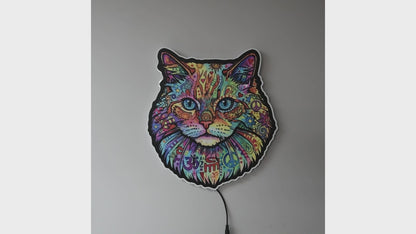 A colorful LED wall light turned off then on shaped like a cat's face, featuring a vibrant multicolor paisley and floral pattern with blue eyes, glowing against a dark gray wall.