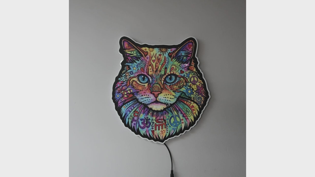 A colorful LED wall light turned off then on shaped like a cat's face, featuring a vibrant multicolor paisley and floral pattern with blue eyes, glowing against a dark gray wall.