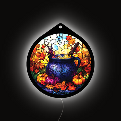 Witch's cauldron LED sign glowing on a wall, pumpkins and fall leaves lit up