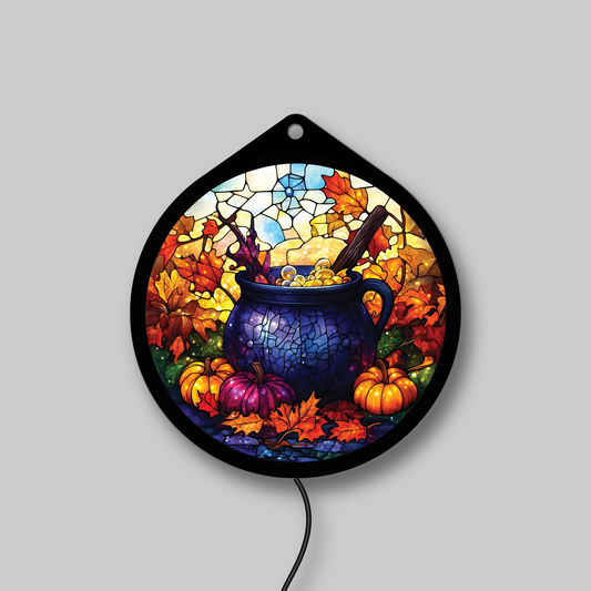 Witch's cauldron LED sign glowing on a wall, pumpkins and fall leaves