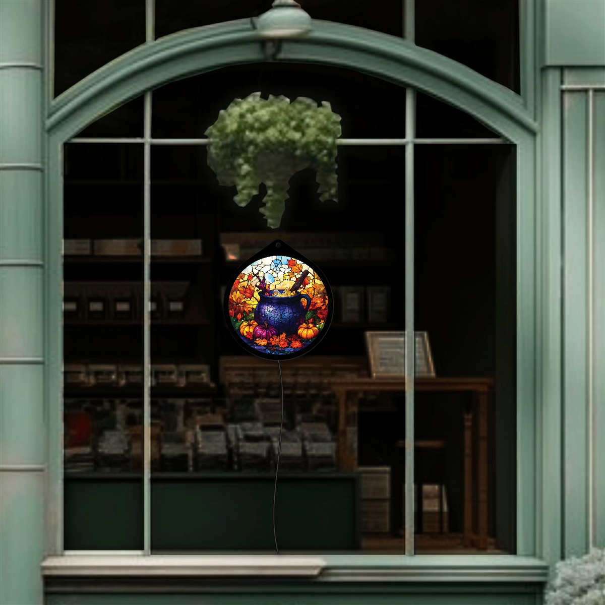 Witch's cauldron faux stained glass sign with pumpkins, hanging in storefront window, lights off