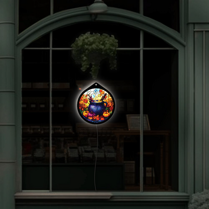 Witch's cauldron LED sign glowing in a shop window, pumpkins and fall leaves lit up